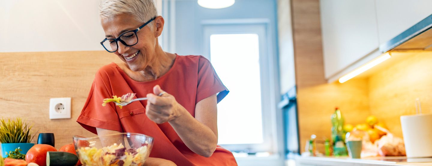 Middle-aged woman eating salad at kitchen counter. 