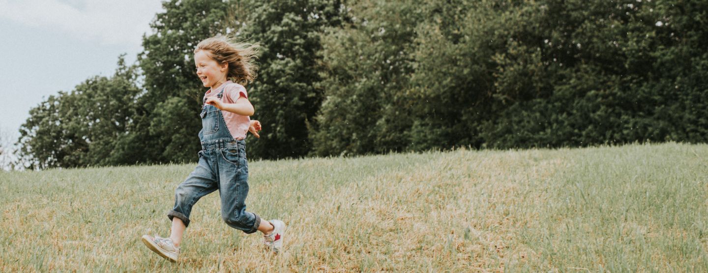 Young girl running down hill outside. 