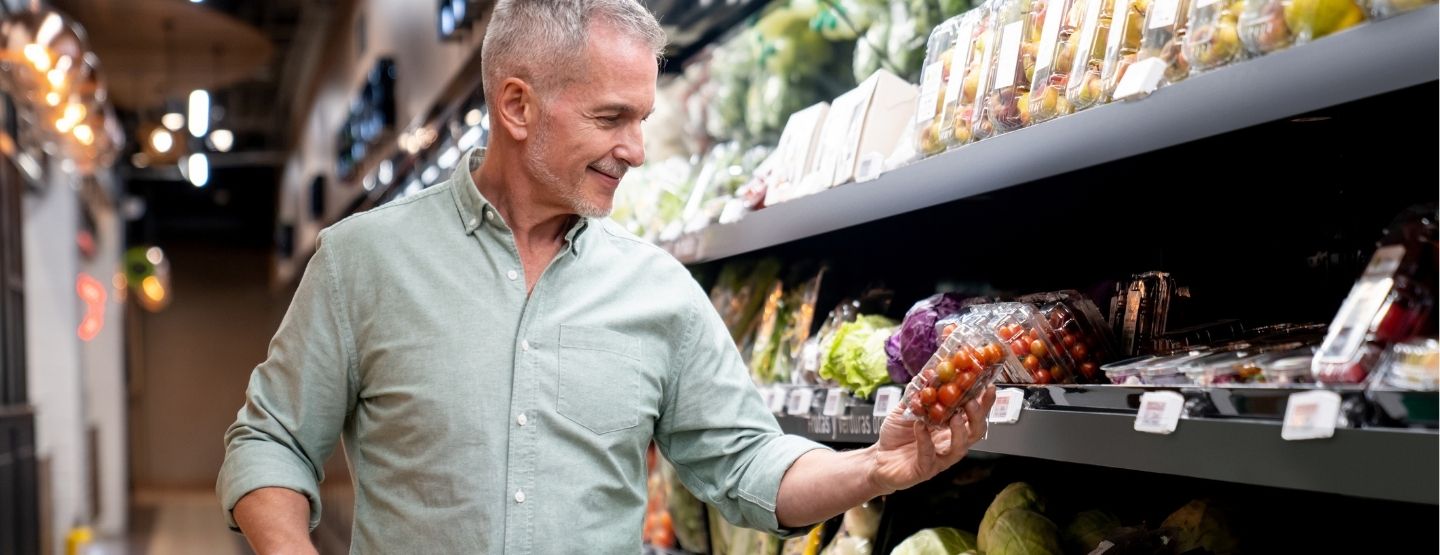 Middle aged man holding tomatoes in the produce aisle.