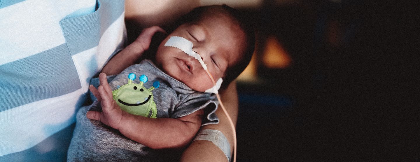 Baby with oxygen cords sleeping in the arms of a loved one.