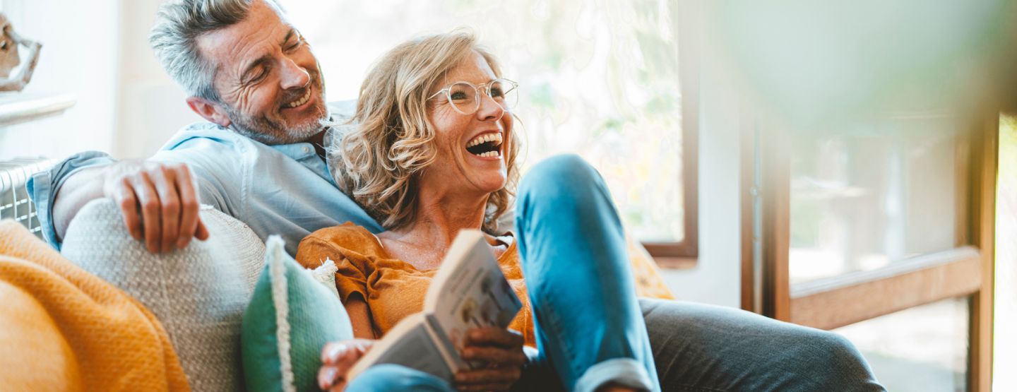 Middle aged couple laughing together on the couch.