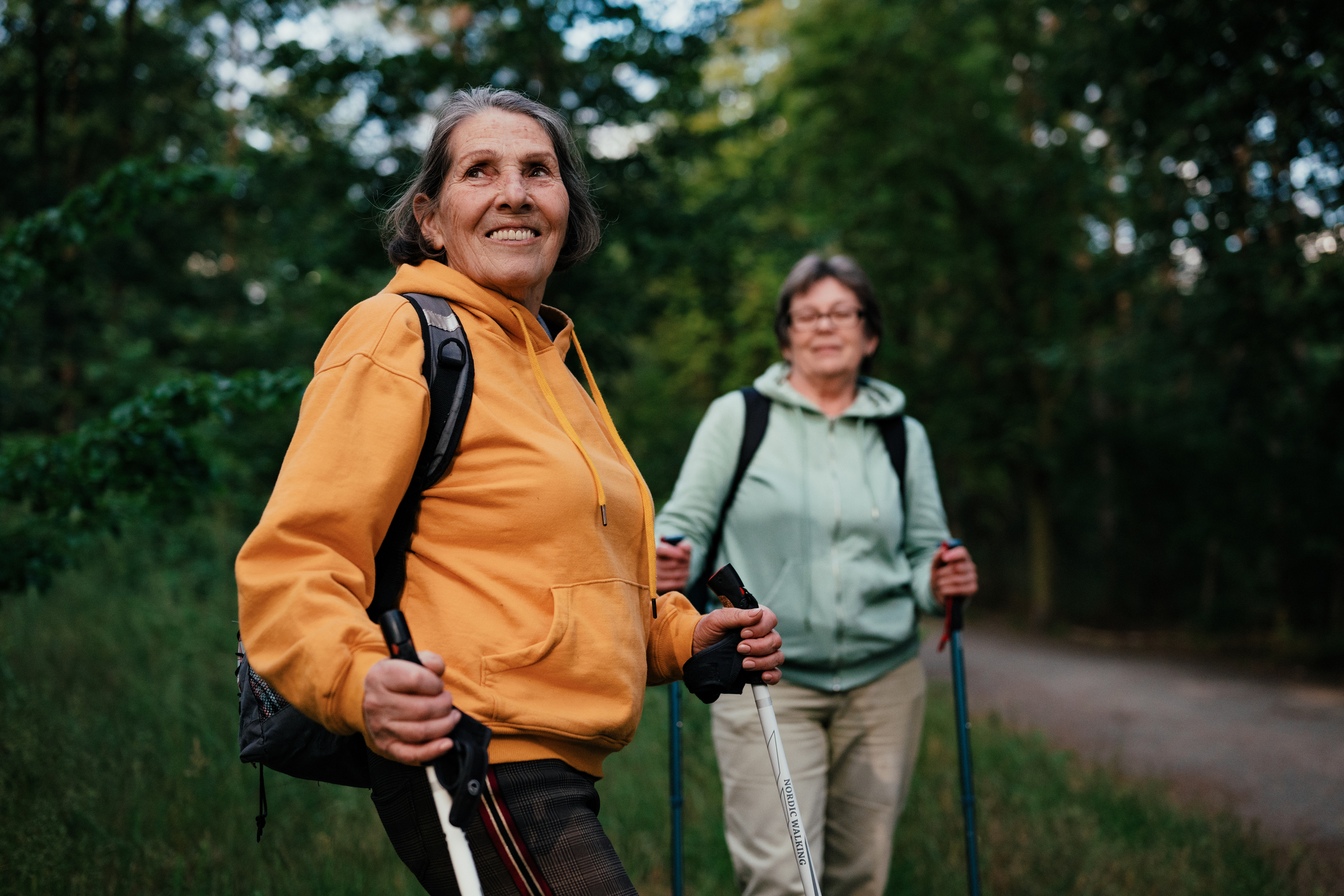 Two older women walking outdoors with walking sticks