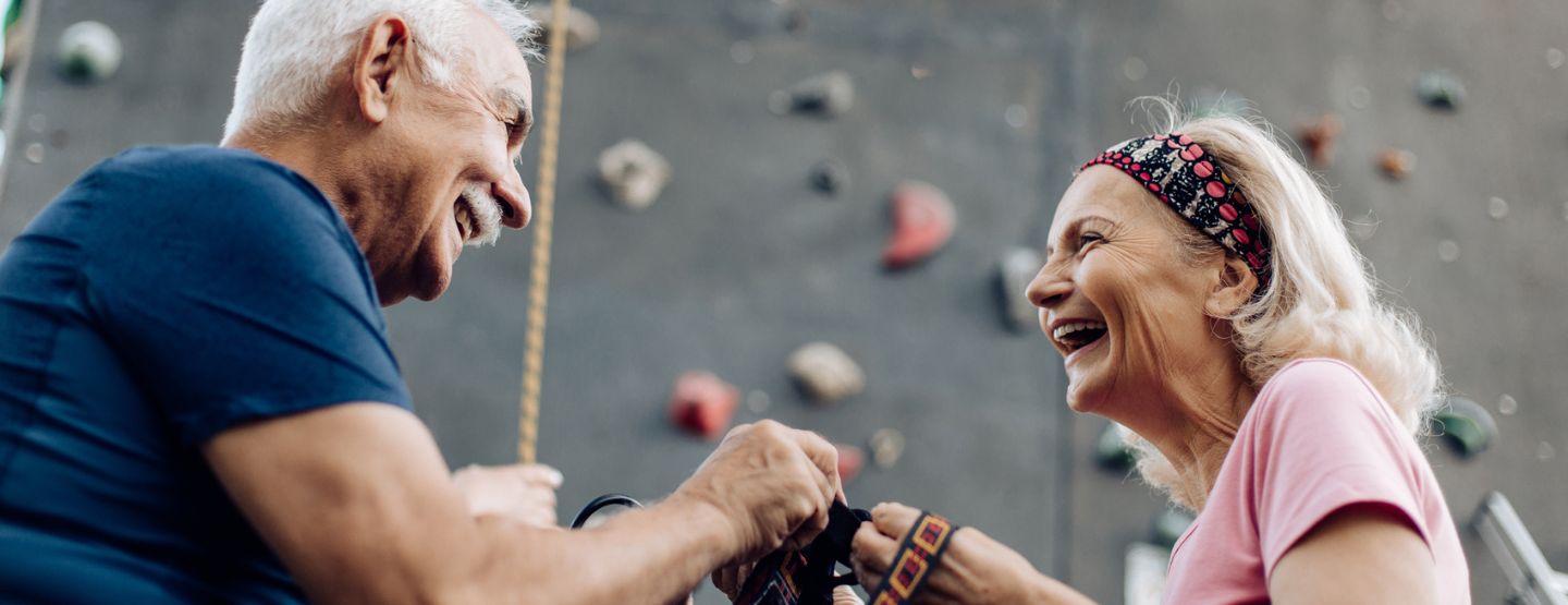 Mature couple smiling at each other in front of rock climbing wall. 