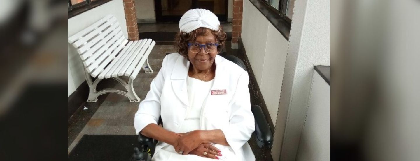 Anna Gardner, a 95-year-old Black woman with glasses, smiling and sitting in her wheelchair in an all-white outfit and hat.