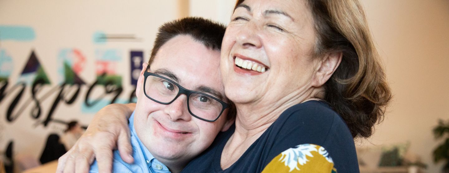 A woman hugging a young man with Down Syndrome.