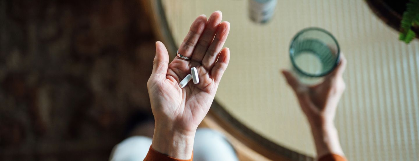 Woman holding supplements in one hand and a glass of water in the other.