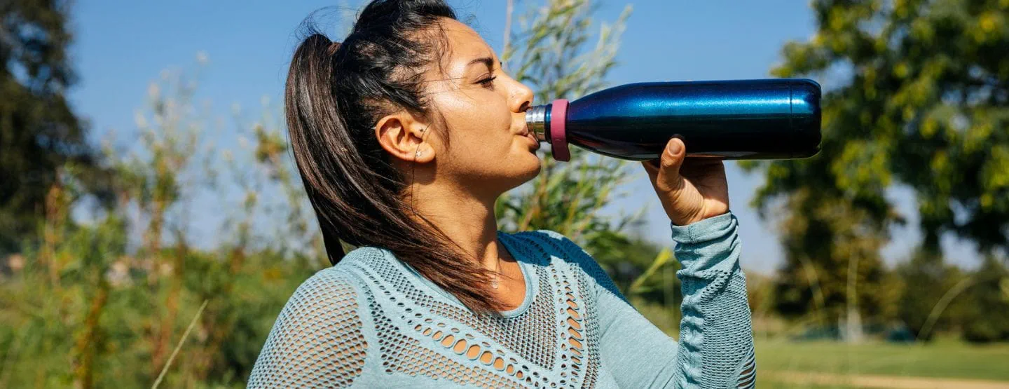 Woman drinks from water bottle while outside working out. 