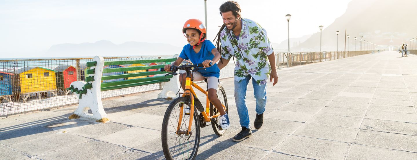 Boy riding a bike with help from his dad 