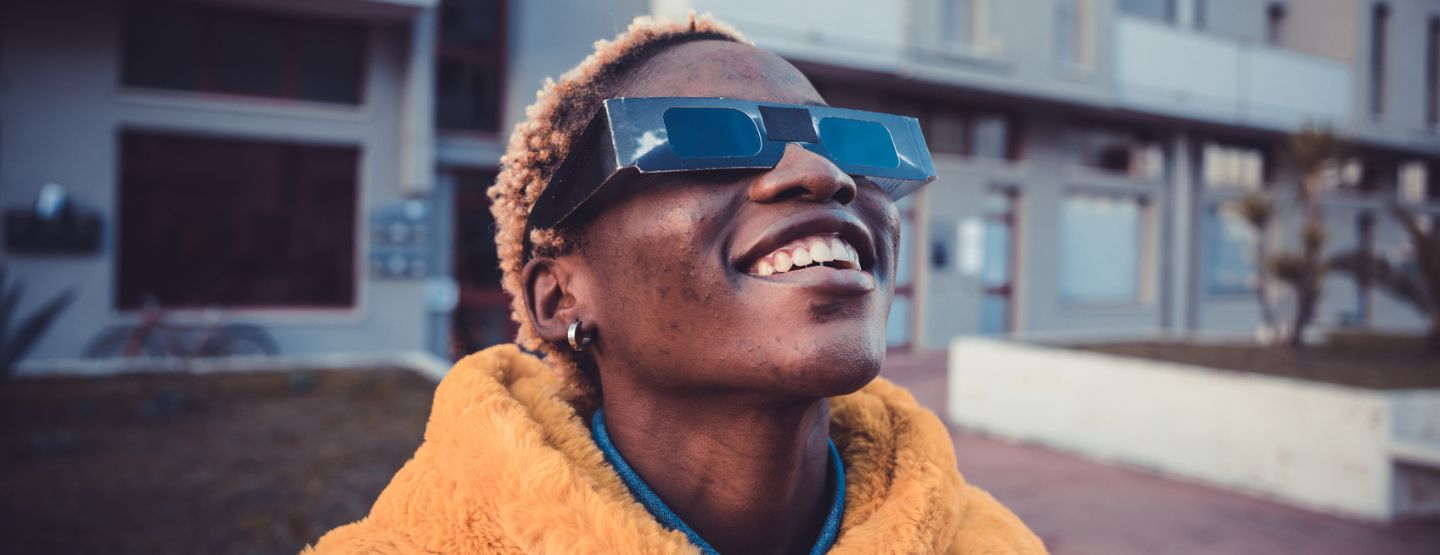 Woman wearing eclipse glasses smiles at the sky.