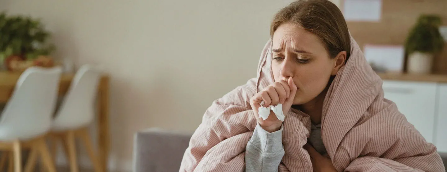 Young woman coughing and sitting under the duvet at home.