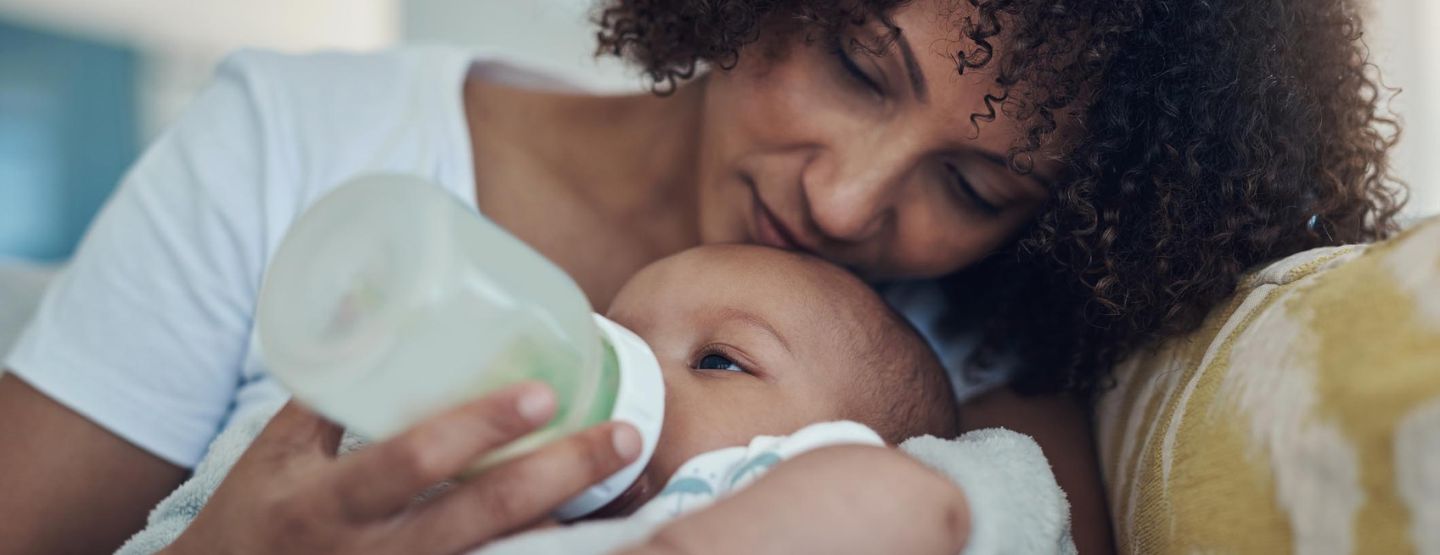 A mom laying in bed bottle feeding her infant.