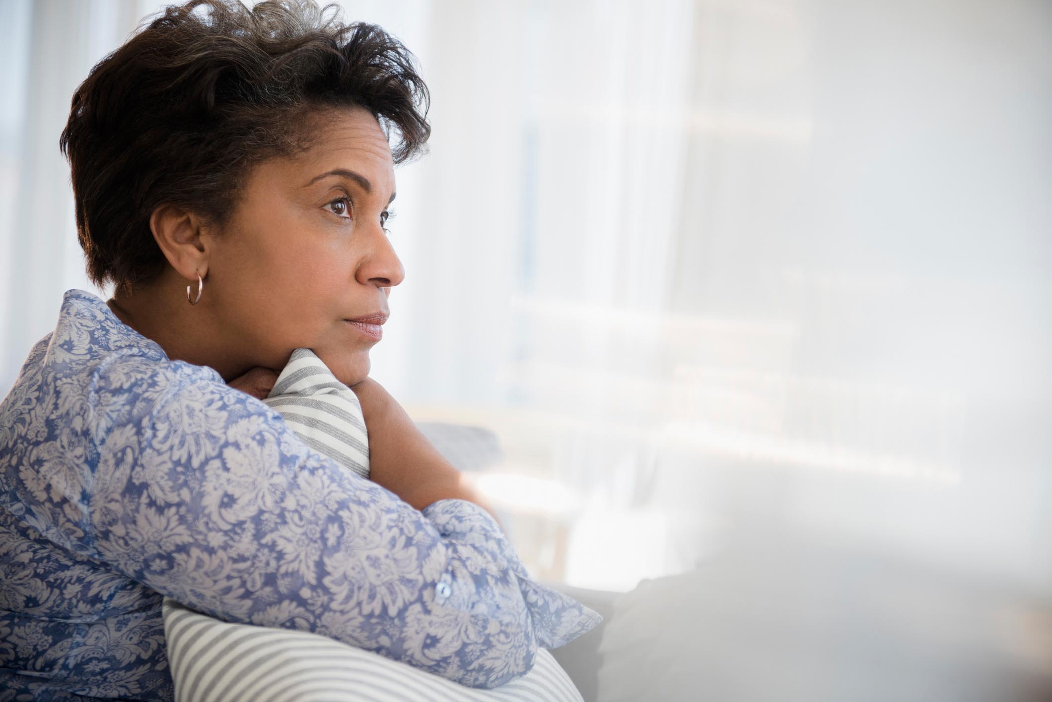 A picture of a woman sitting while hugging a pillow and staring out the window