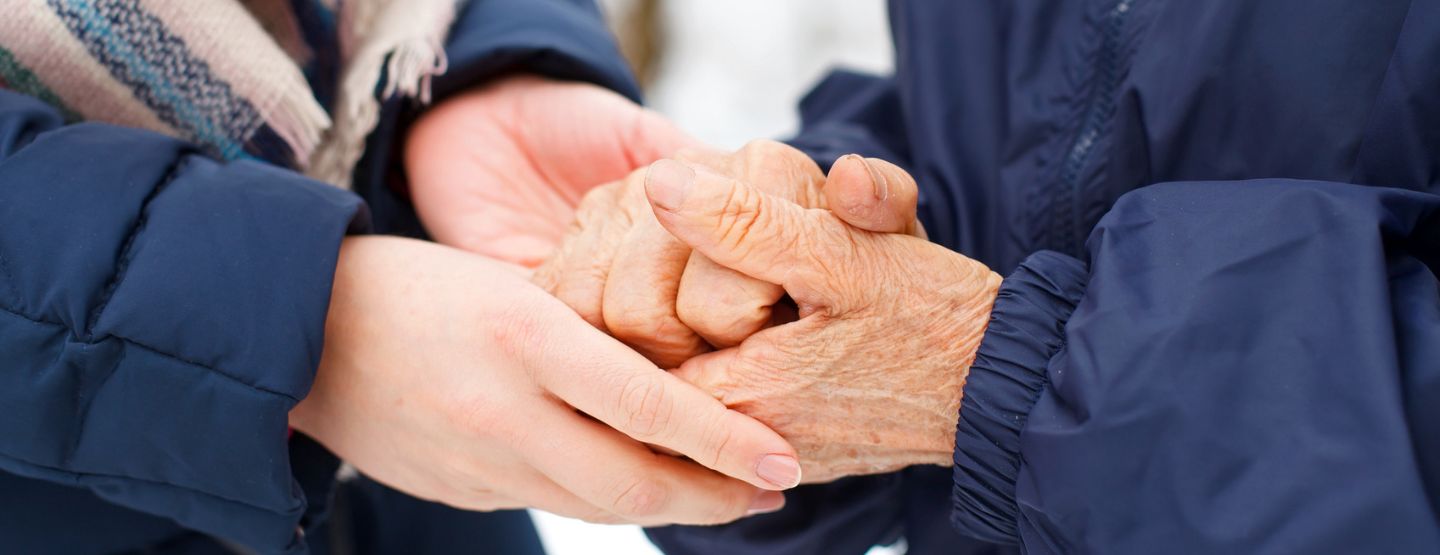 Pair of younger hands holds pair of older hands outside in winter. 
