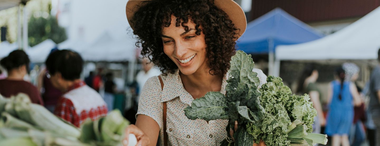 Woman smiling while picking out bunches of kale at a farmers' market. 