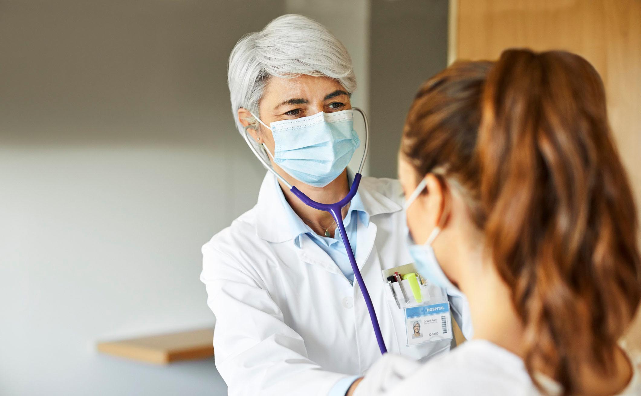 Medical worker examining female patient through stethoscope in ICU.