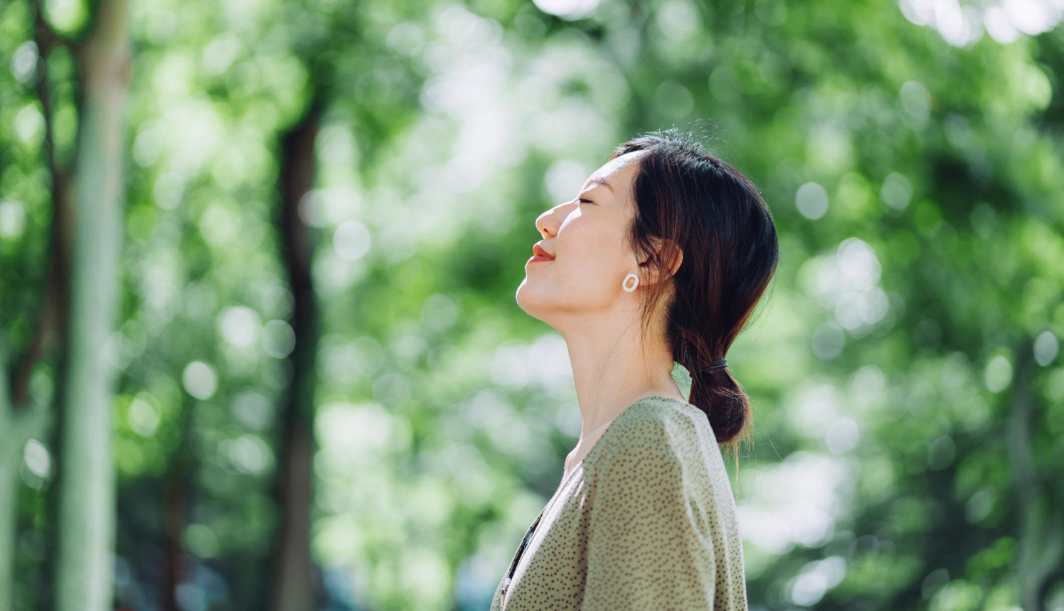 Beautiful young Asian woman meditating in the nature with her eyes closed, setting herself free and feeling relieved.