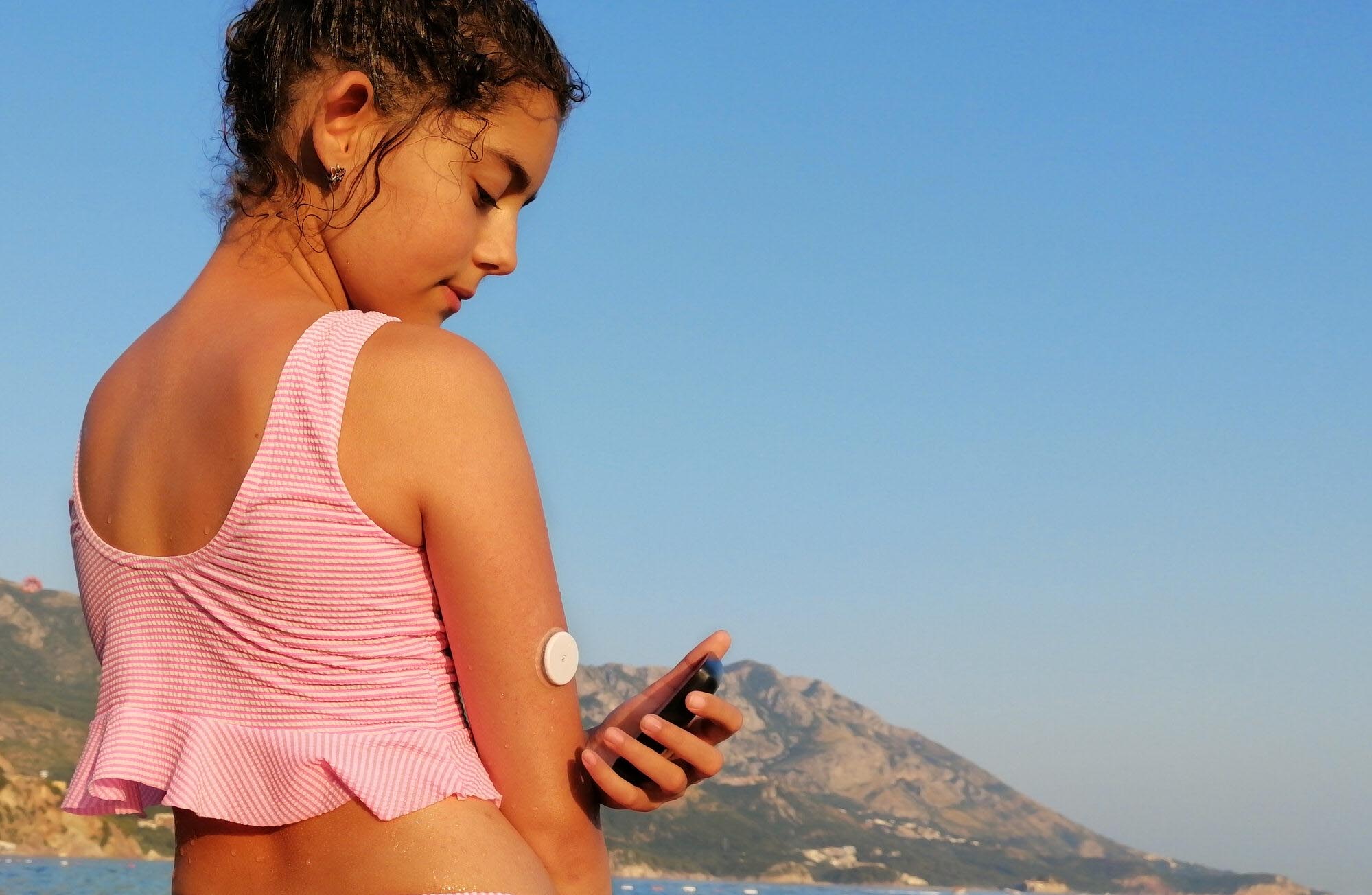 A young girl in a swimsuit checks her glucose level