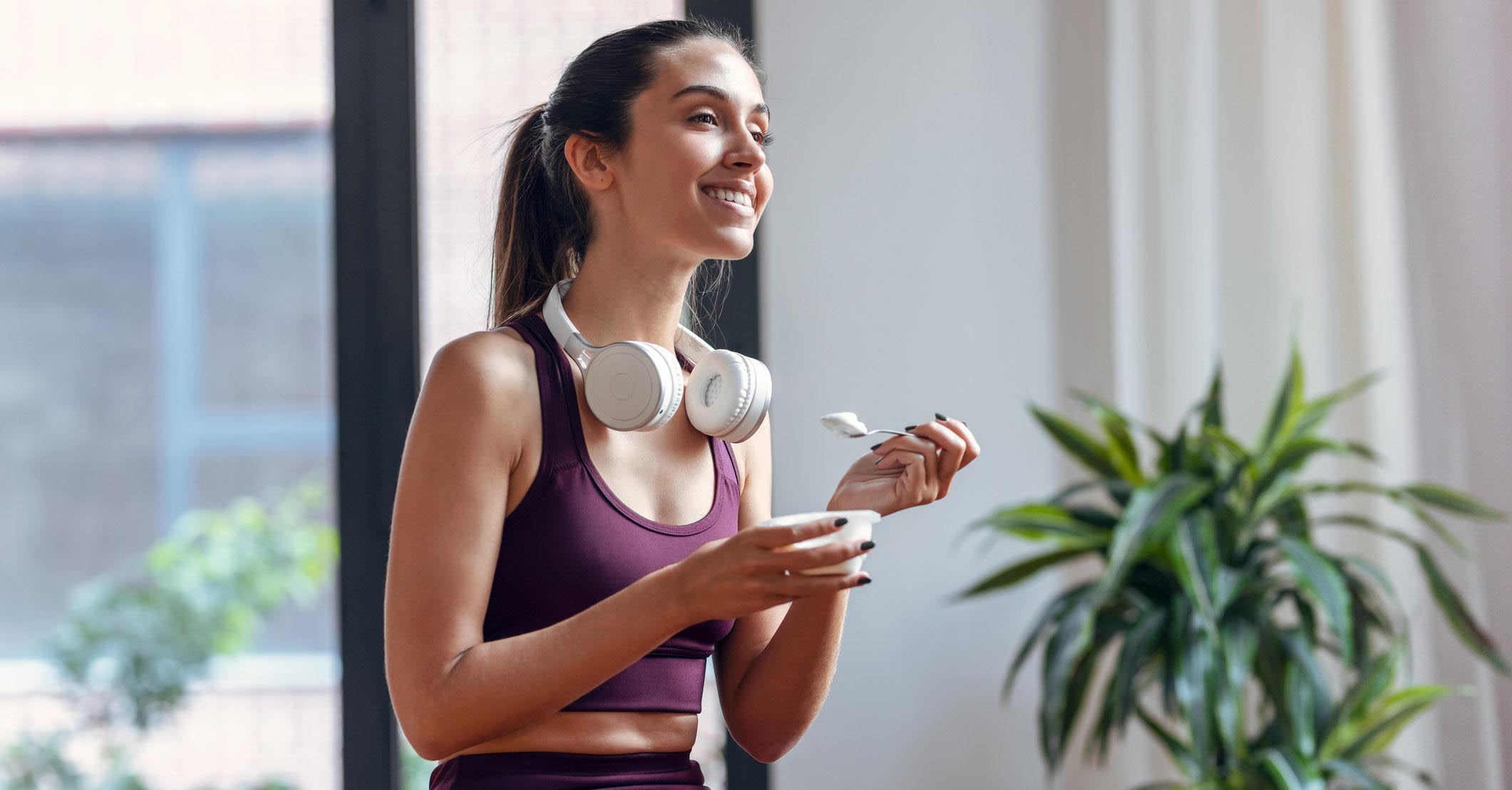 Shot of sporty young woman eating a yogurt while sitting on fitness ball at home.