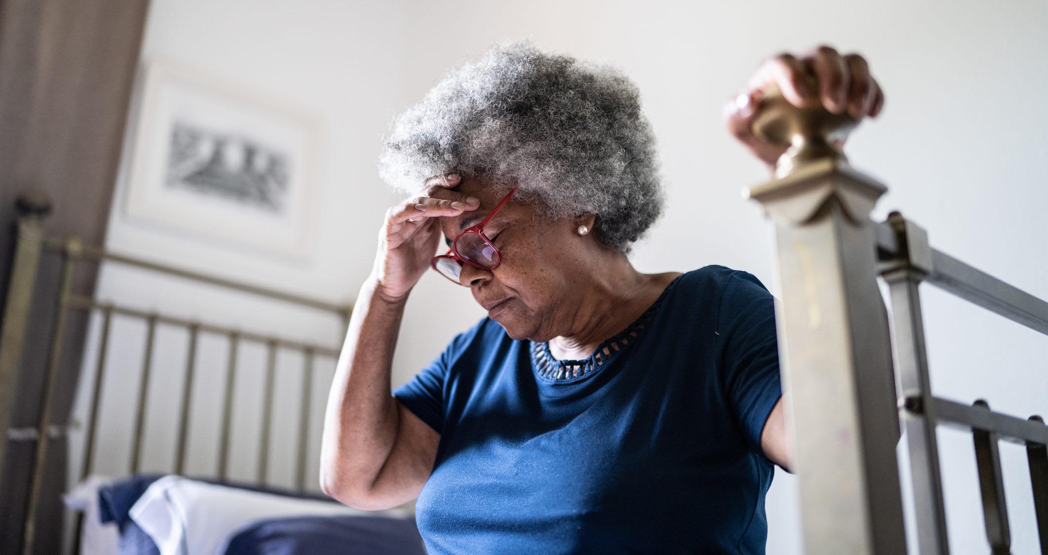 Senior woman with headache sitting in the bed at home