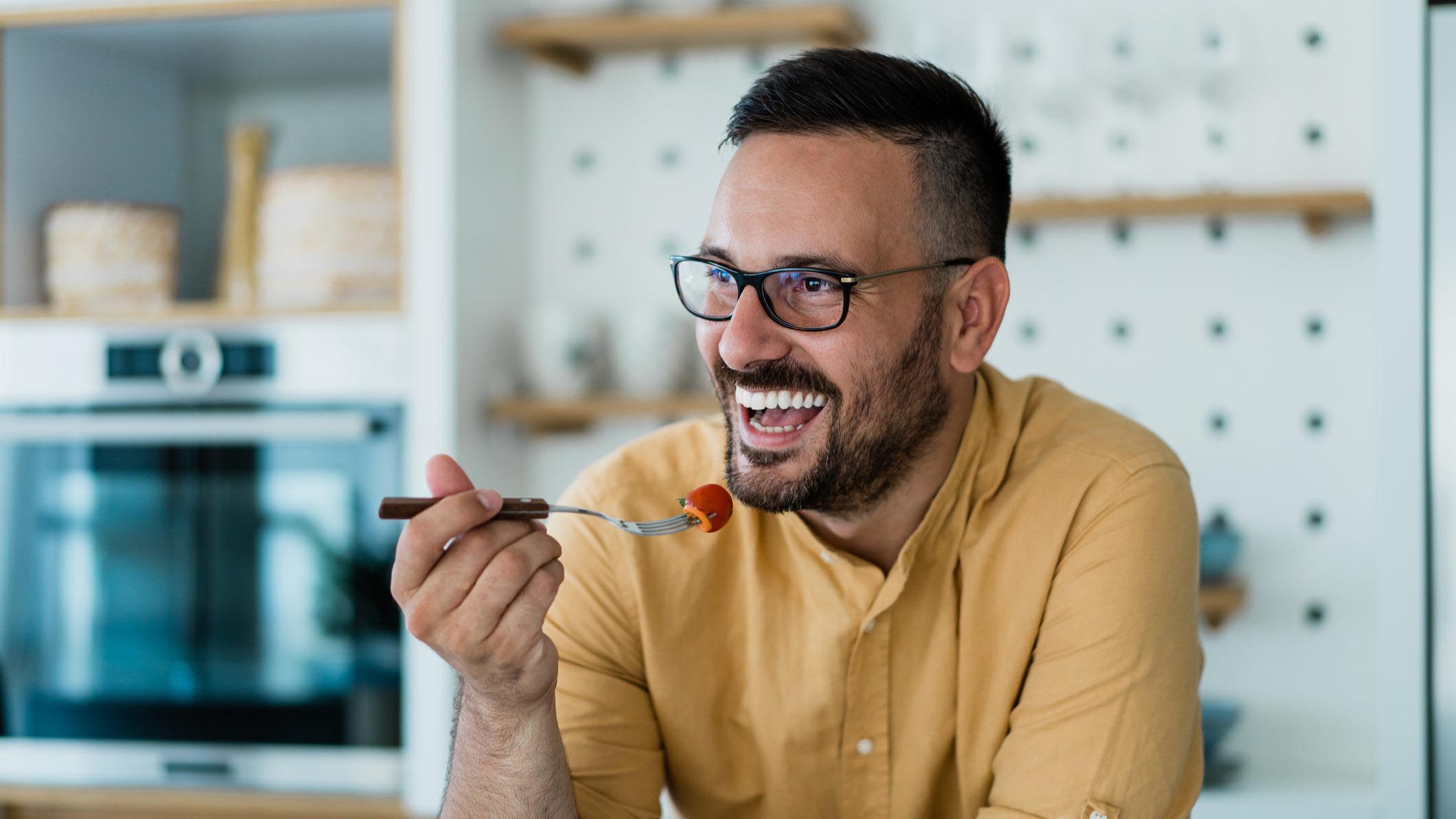 Shot of a cheerful young man eating a healthy salad for lunch or dinner at home.