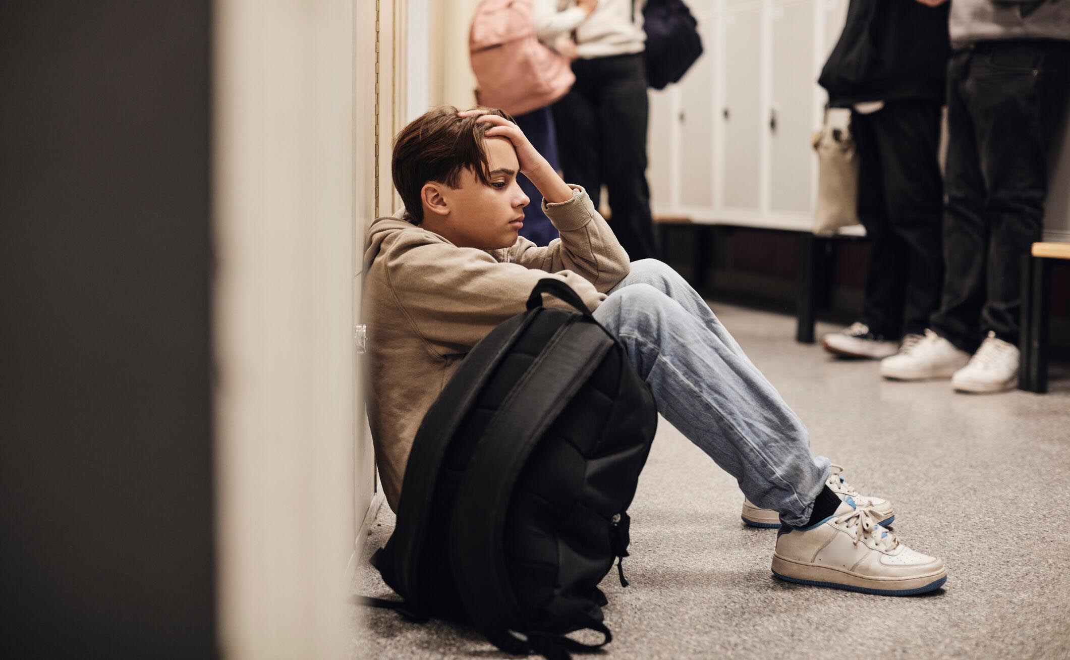 A stressed out young boy sits on the ground in front of his locker at school. 