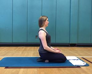 Woman kneeling on a mat facing her left side with her hands resting on her lap