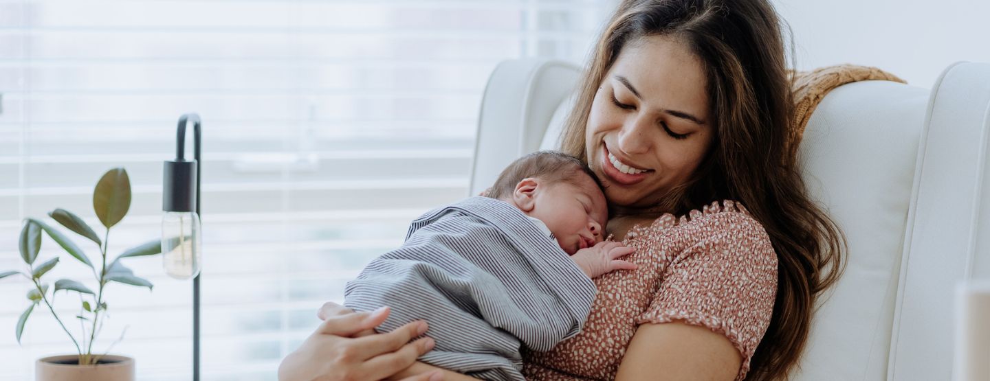 A mother sitting in a chair with her newborn sleeping on her chest.