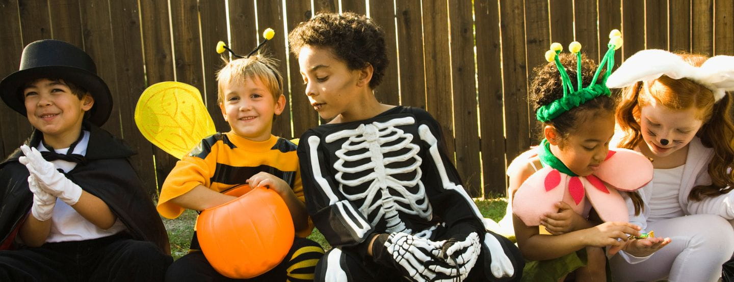 Children in Halloween costumes sitting on sidewalk