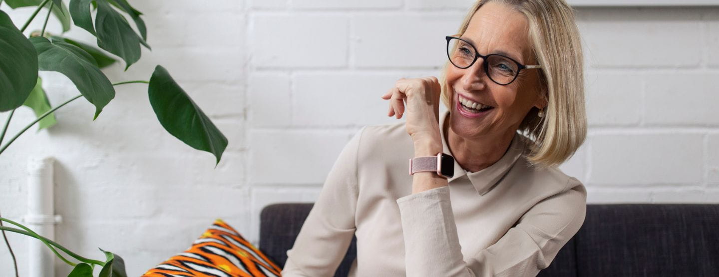 Mature woman wearing smart watch, smiling and sitting on couch. 