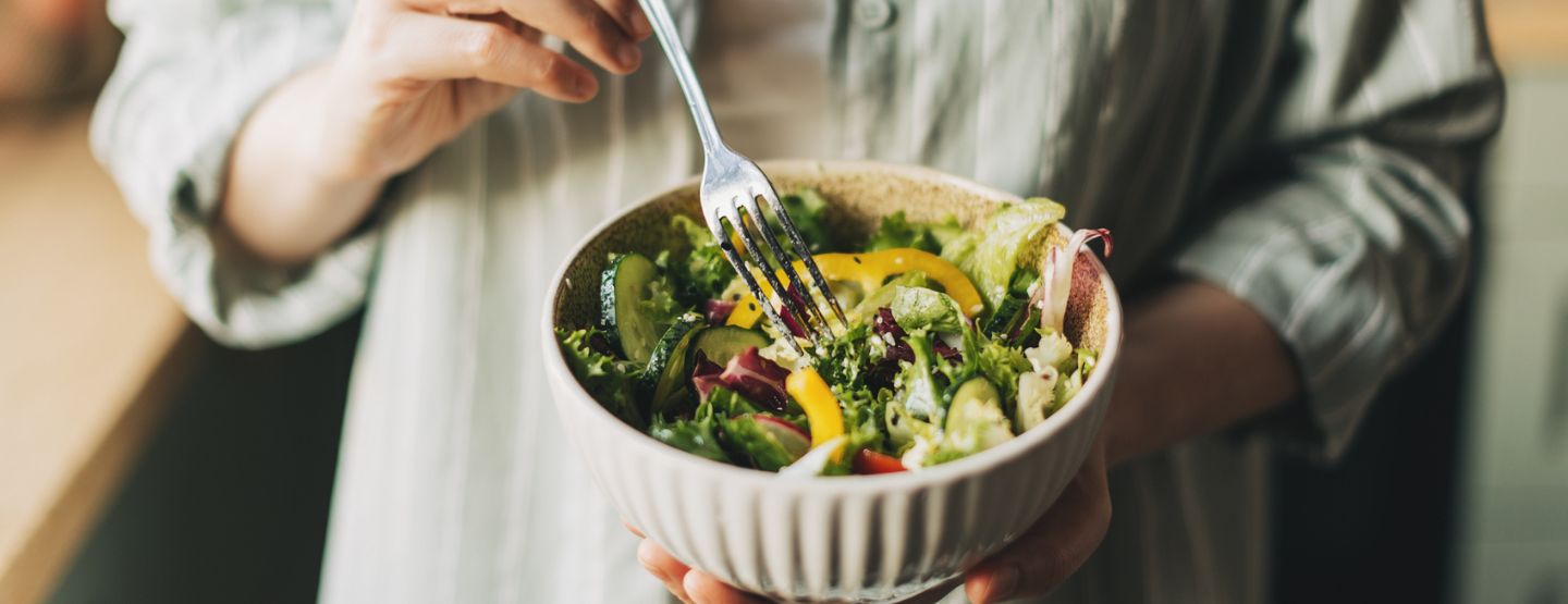 Hands hold leafy greens salad topped with fresh vegetables. 