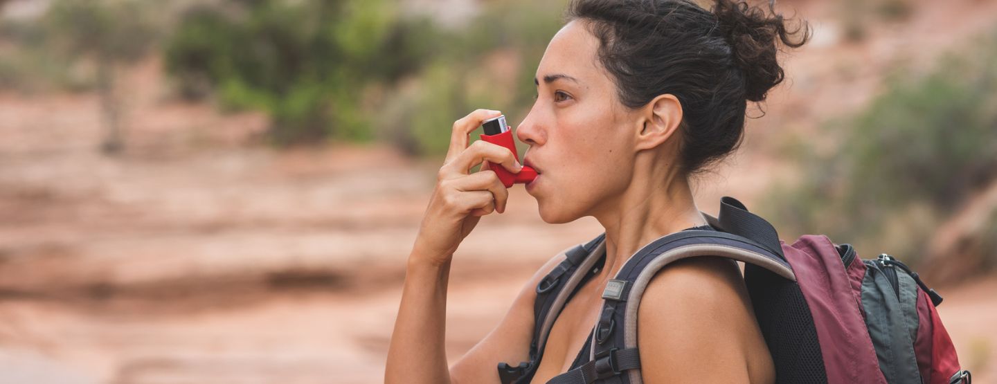 Middle-aged woman using inhaler while on hike in the high desert. 