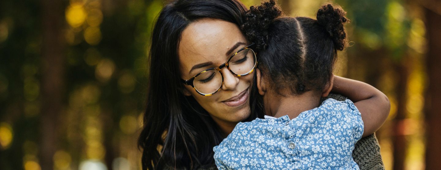 Woman wearing glasses hugging little girl.