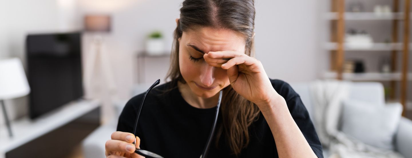 Woman takes glasses off to rub eyes in discomfort. 