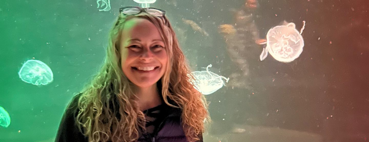 Kami Moon smiling and posing in front of an aquarium tank with jellyfish.