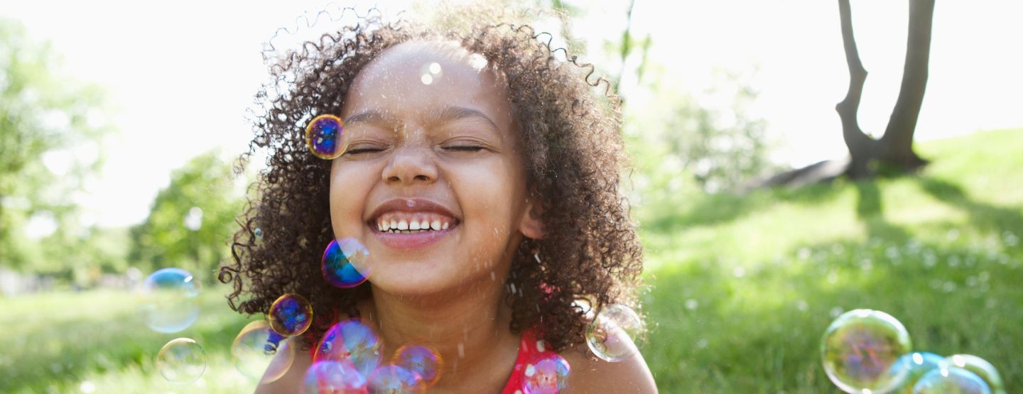 Young girl smiles while bubbles float around her.