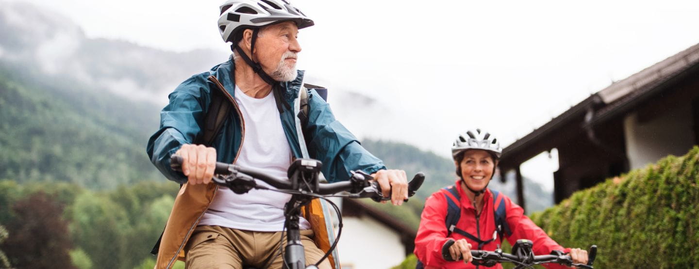 Mature man and woman riding bikes outside. 