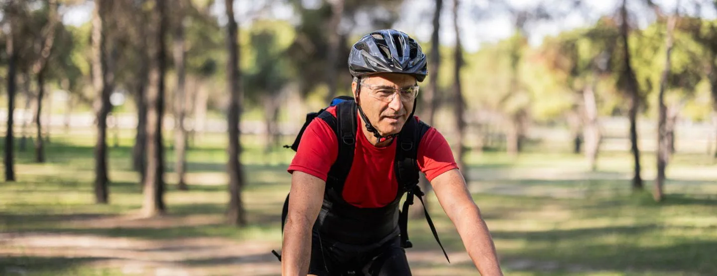 Man in his 60s wearing a helmet and riding his bike among trees.