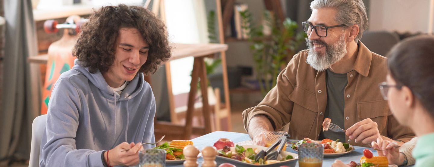 Teenage boy with father and younger sibling at the table eating dinner.