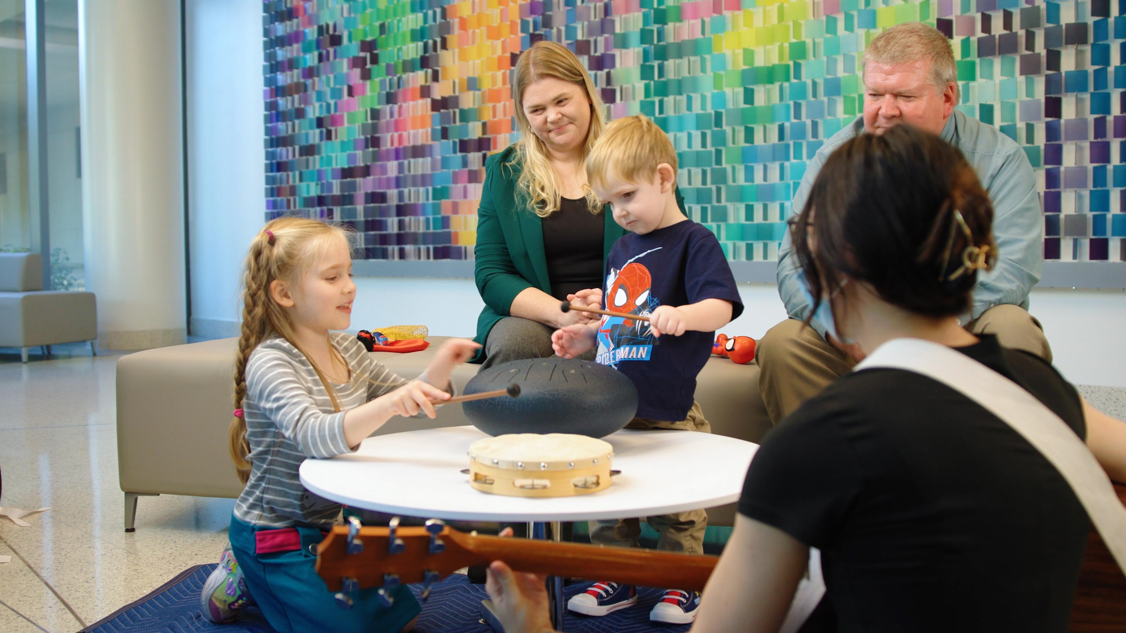 A family of four (mother, father, son, and daughter) attend a music therapy session with the music therapist.
