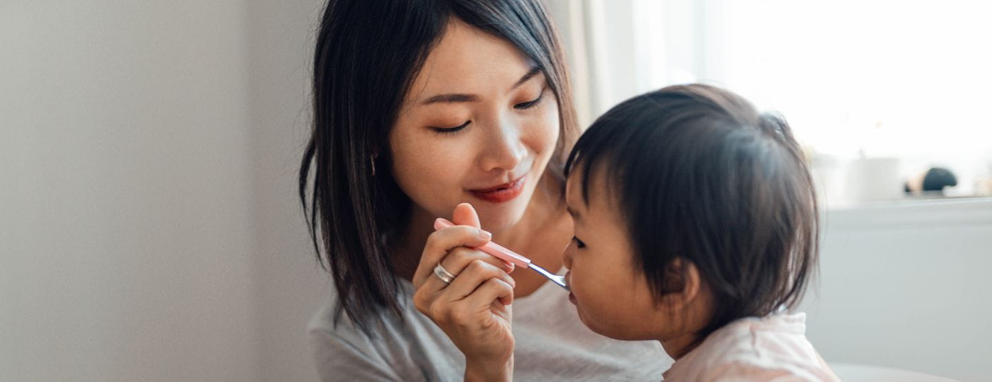 Young Asian mom spoon feeds baby.