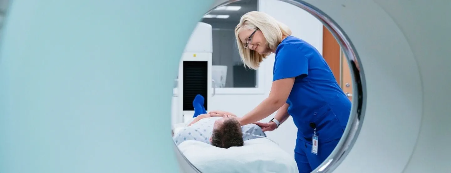 Smiling tech in blue helps laying man prepare to go into the MRI machine