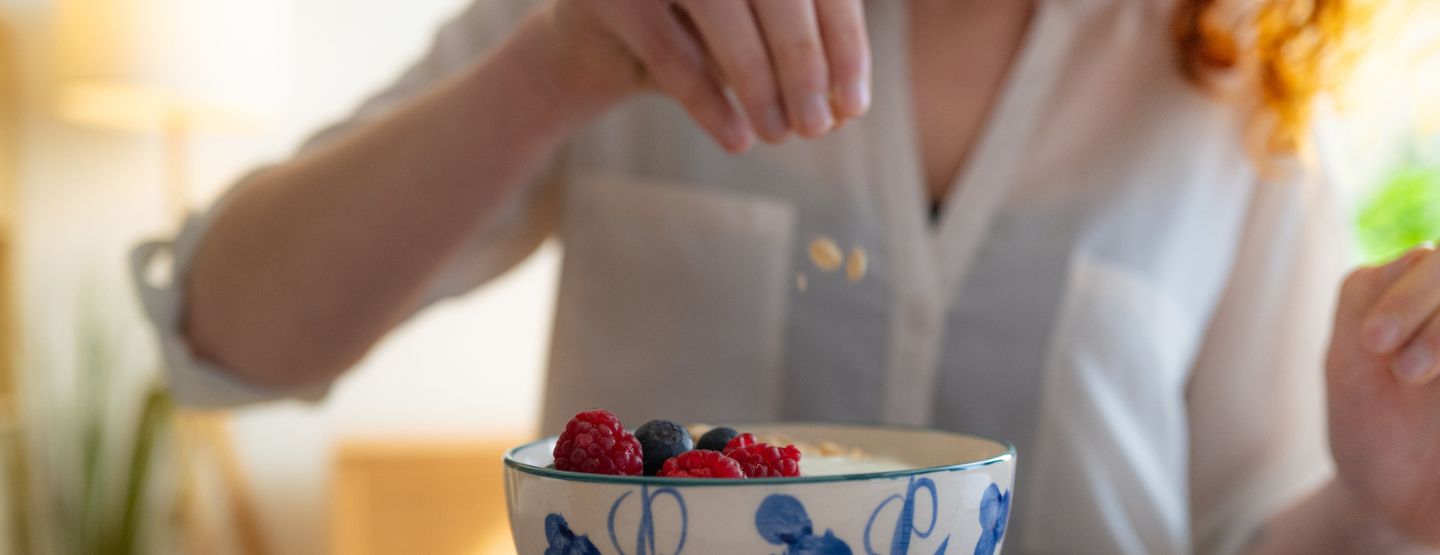 Women dropping granola into a bowl of yogurt