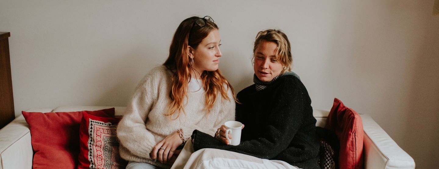 Two women sitting closely on the couch having a serious conversation.