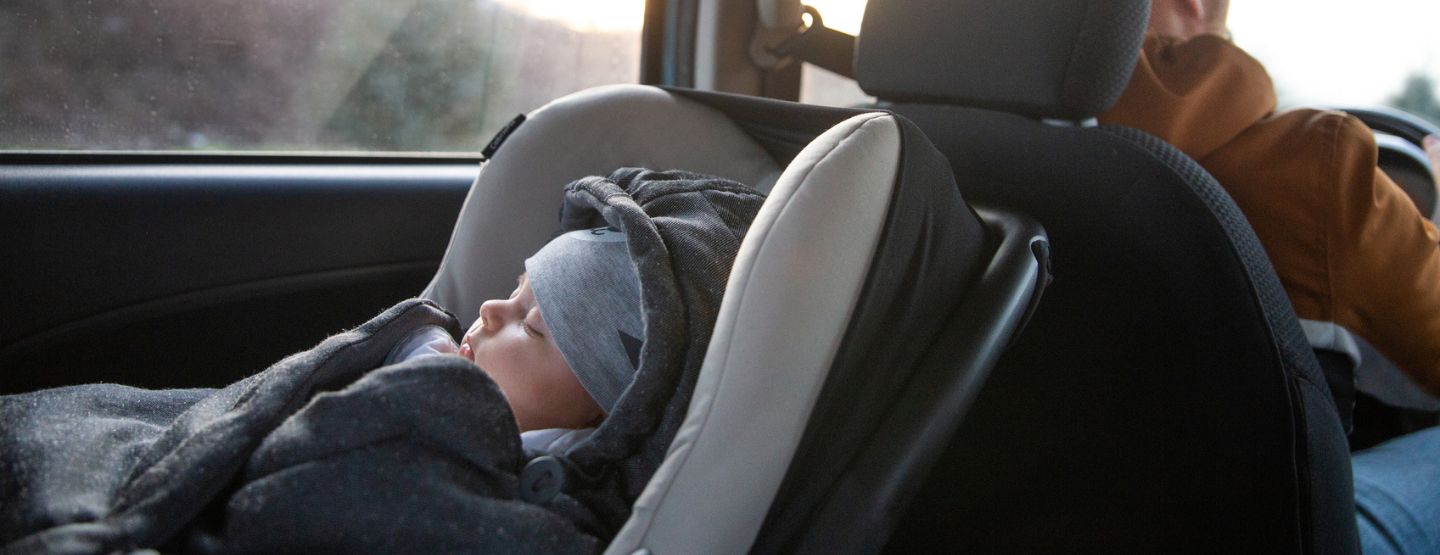 Baby sleeping in car in car seat with car seat cover and father driving. 