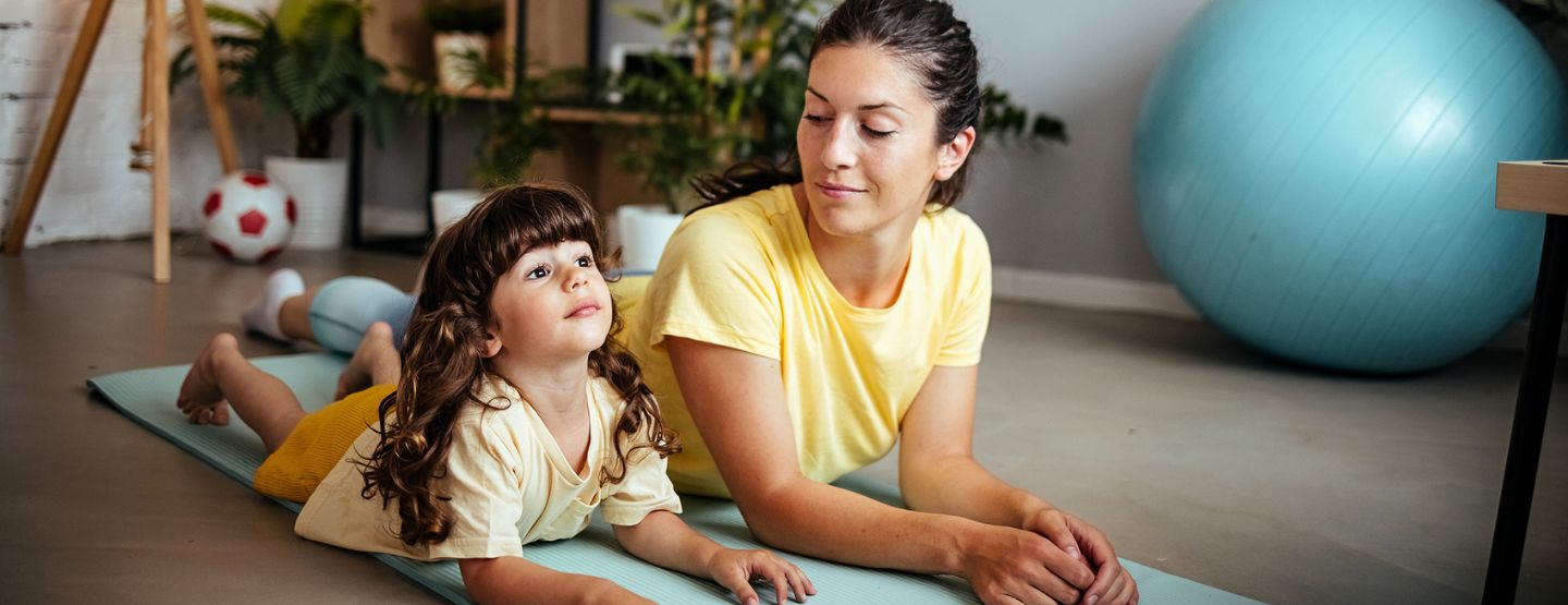 Mother and young daughter laying on yoga mat in yoga pose. 