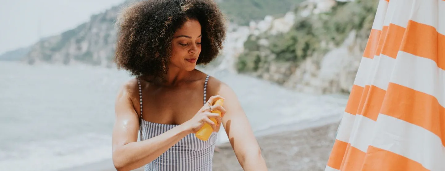 Woman spraying sunscreen on arm while on the beach. 