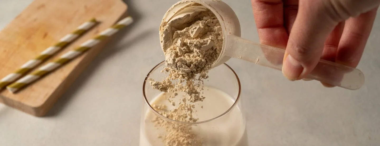 Scoop of protein powder being added to glass of milk.