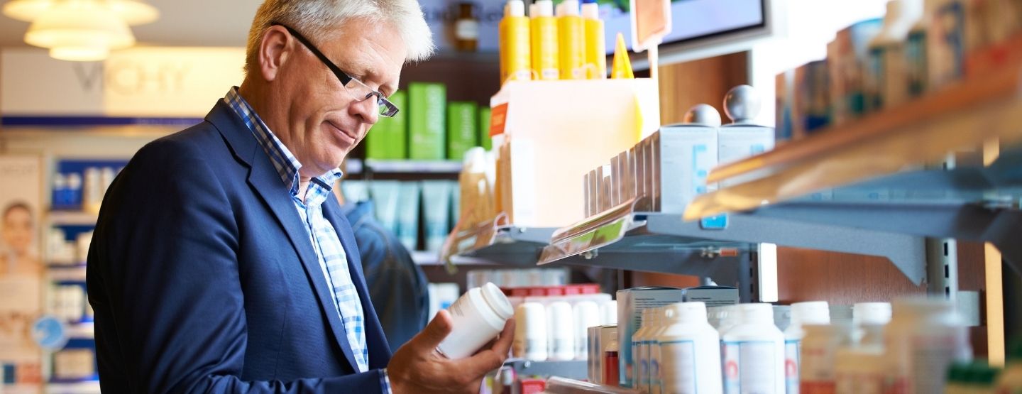 Older man with glasses in a suit looking at a container in a store aisle.
