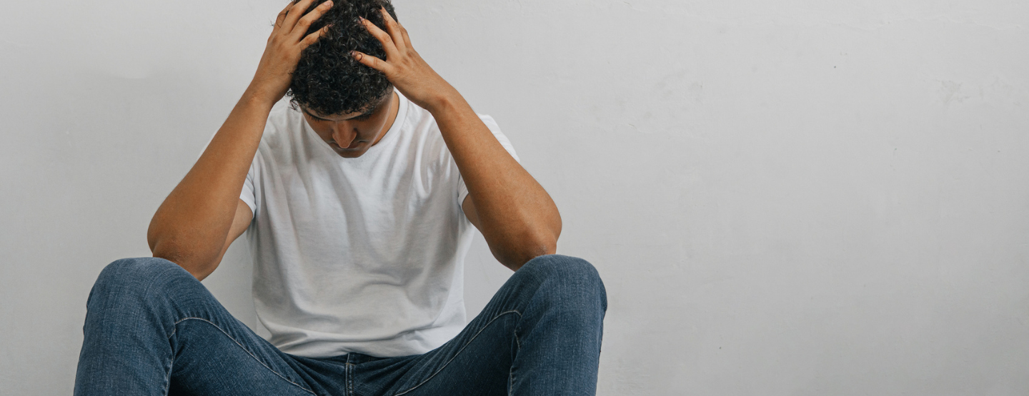 Young man crouched over in distress with hands on head. 