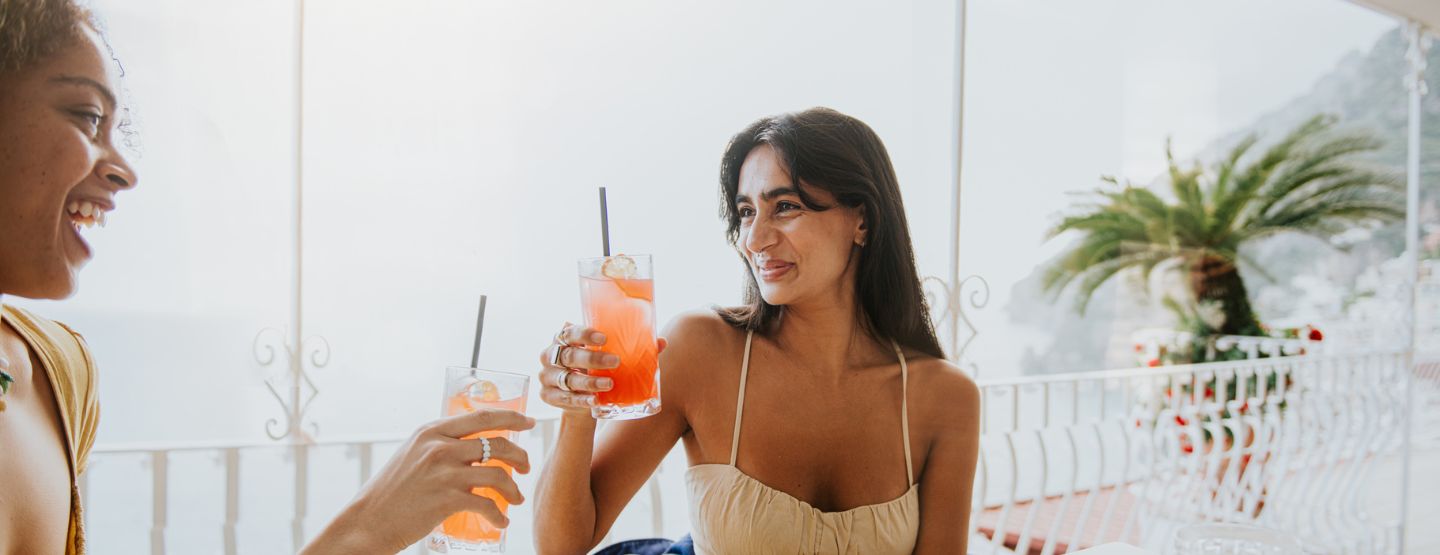 Two women sitting on balcony cheers mocktails. 